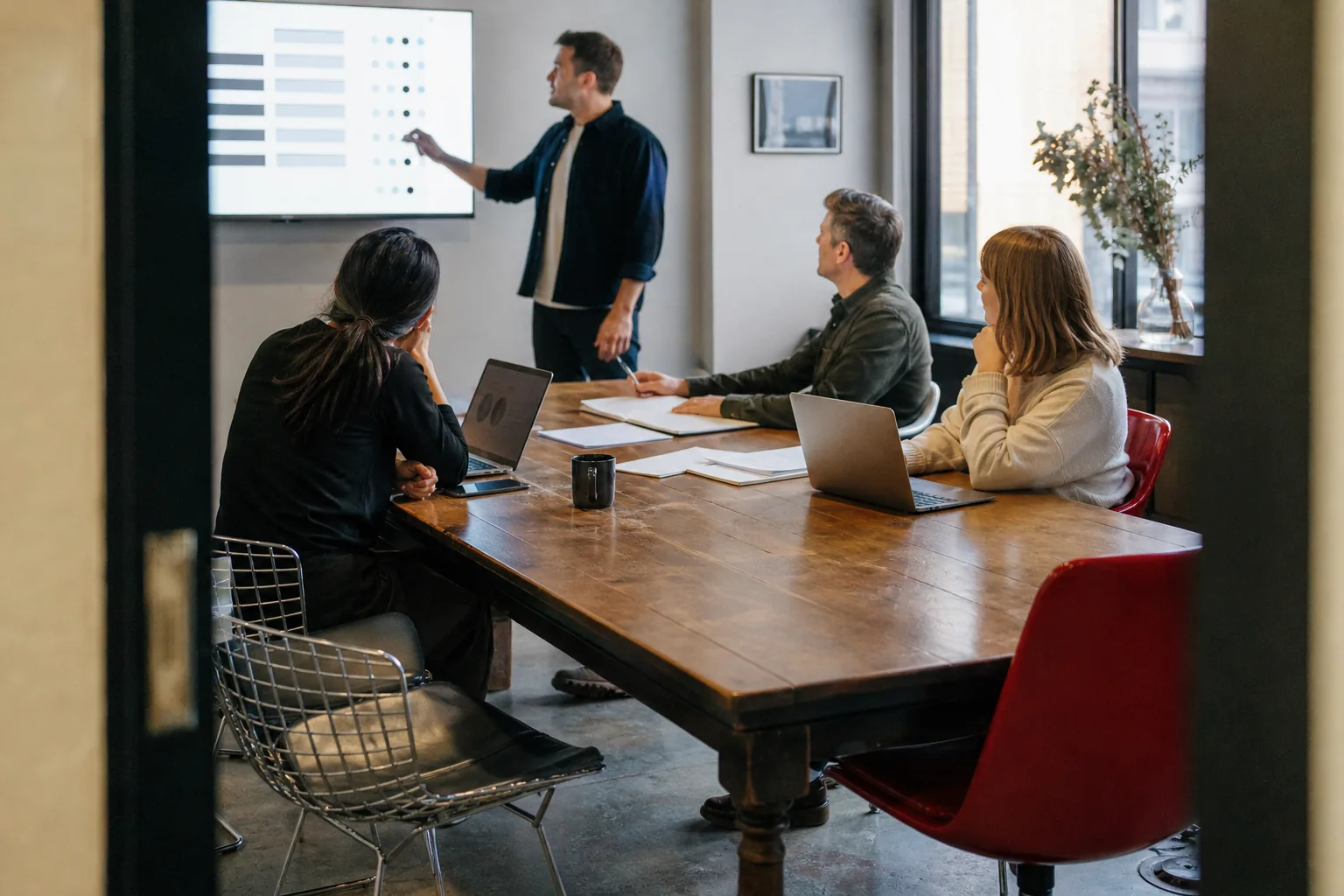 Small team at a meeting table reviewing agent run results on a wall screen