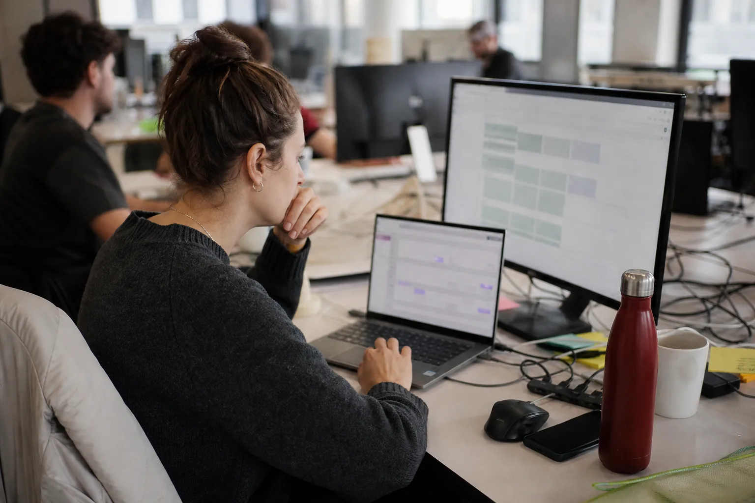 Operations specialist connecting team tools on a laptop with a chat window and a spreadsheet on a second screen