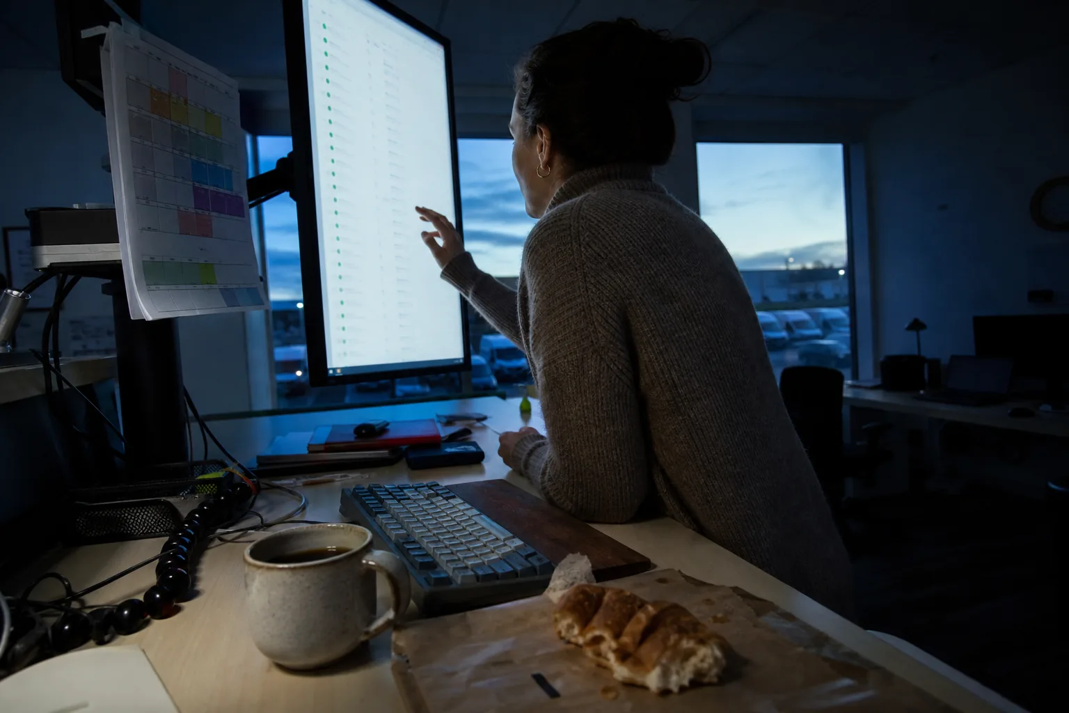 Operations lead at a standing desk reading a finished overnight run log on a large monitor